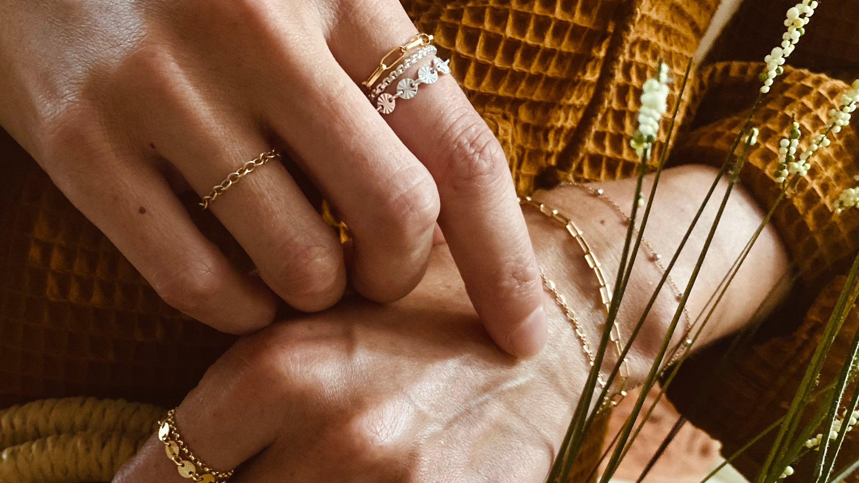 Close-up of hands with gold rings and bracelets, wearing a mustard yellow textured garment.